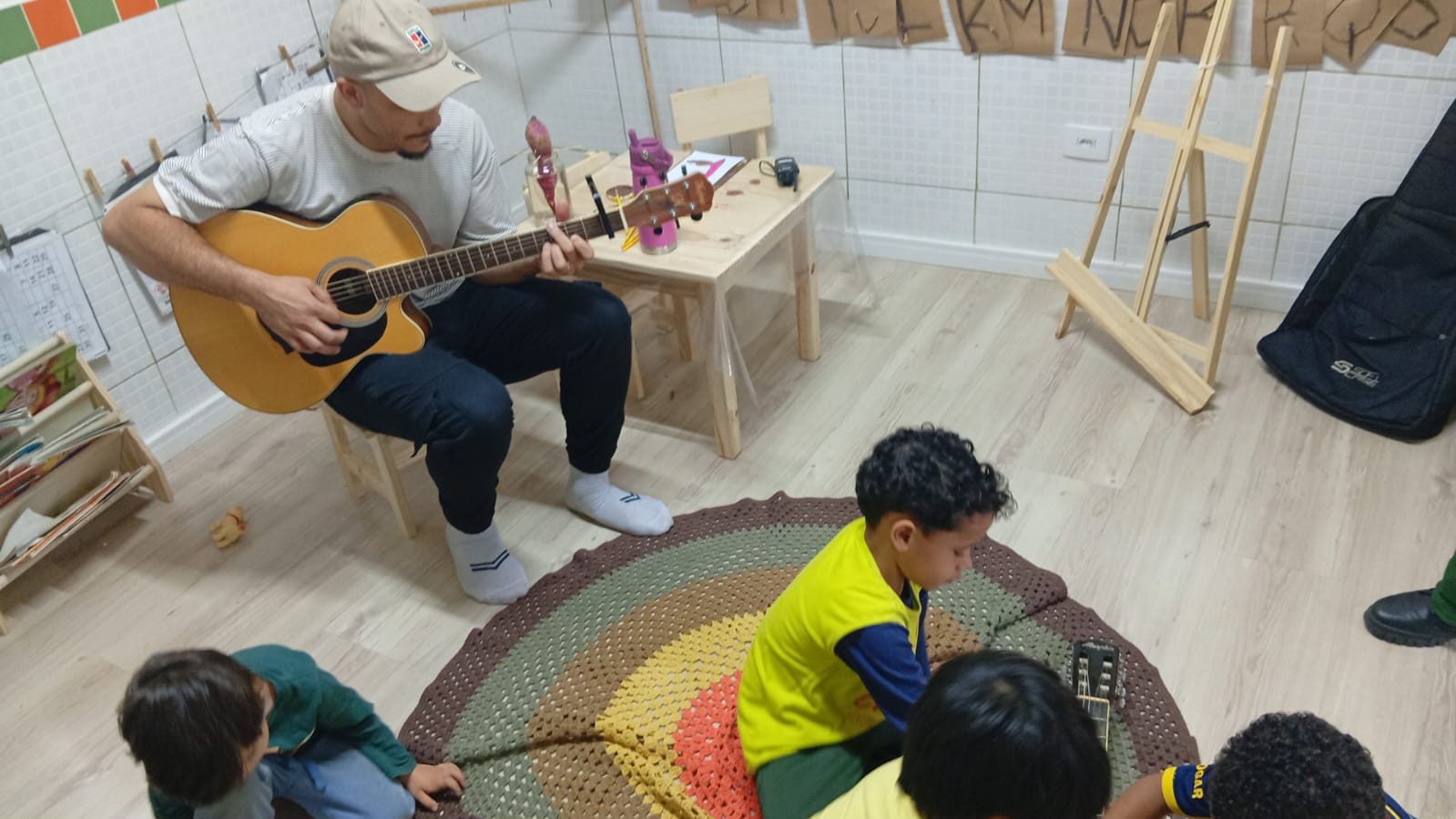 Gabriel tocando violão para crianças sentadas em roda em uma sala de aula